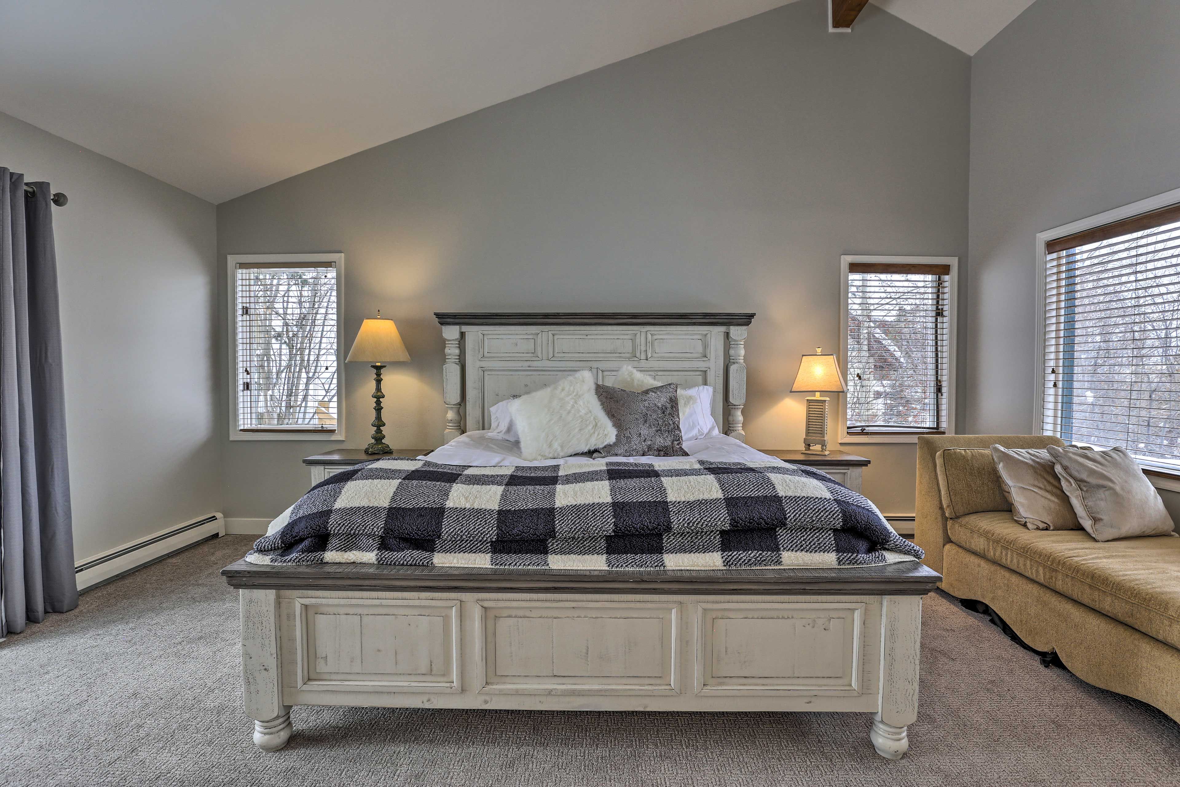 A bedroom with a bed, two bedside lamps, a window with blinds, a couch, and a radiator.
