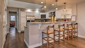 Una cocina moderna con armarios blancos, una isla central con taburetes altos y luminarias colgantes.