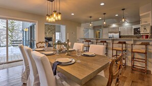 Un comedor moderno con una mesa de madera dispuesta para seis personas, sillas blancas tapizadas e iluminación colgante.