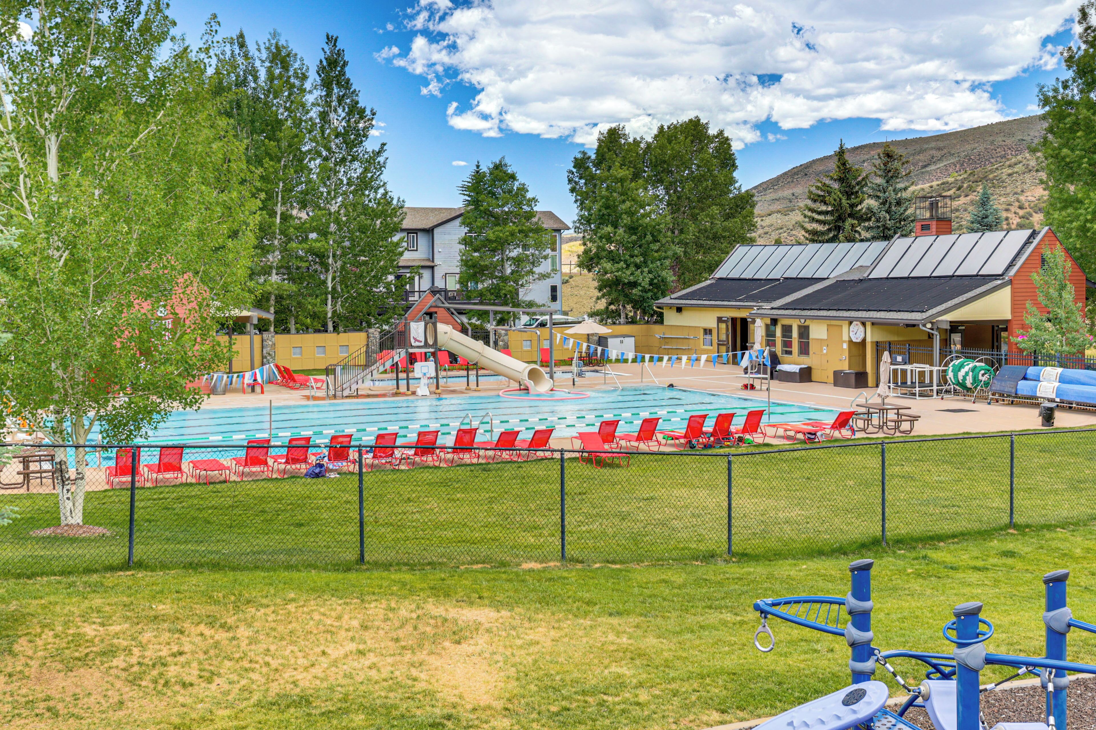Ein Schwimmbecken mit roten Liegestühlen, einer Rutsche und einem eingezäunten Bereich mit einem Spielplatz.
