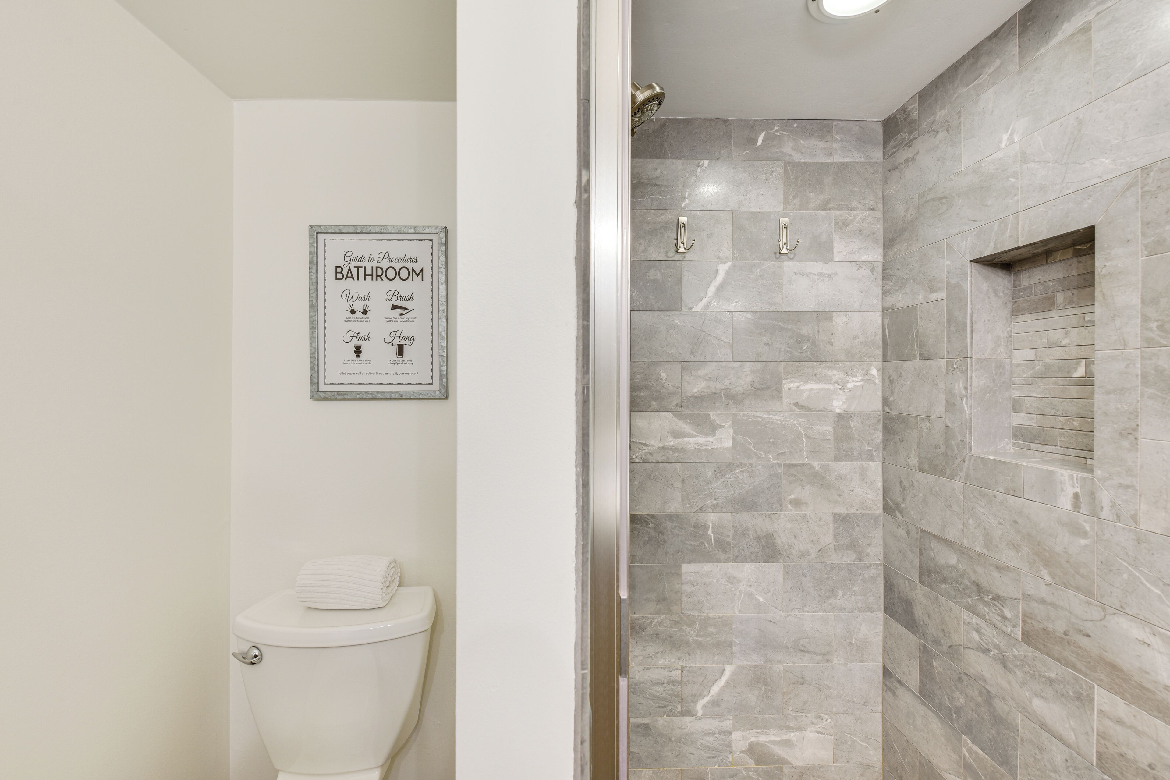 Ein Badezimmer mit Toilette, einer Duschkabine mit Glastür und einem an der Wand befestigten Schild mit Bad-Symbolen.