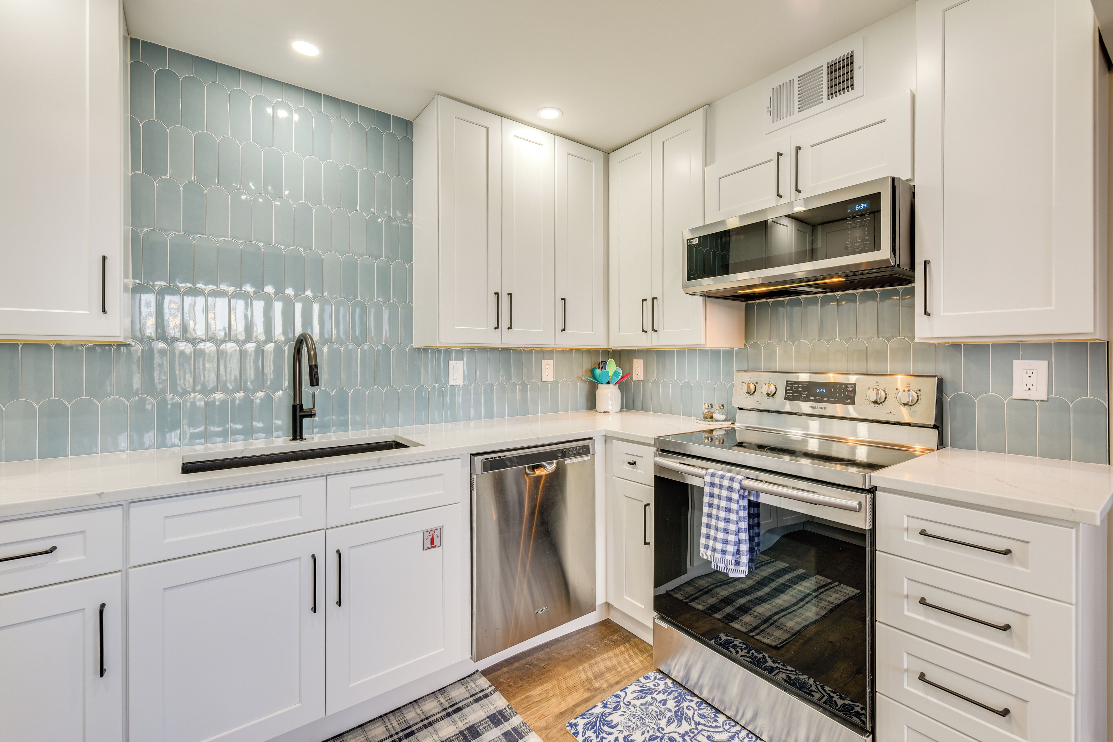 A modern kitchen with white cabinets, stainless steel appliances, and a blue tiled backsplash.