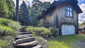 Eine Holzhütte mit einer Steintreppe, die zu einer Terrasse führt, umgeben von üppiger Vegetation und hohen Bäumen.