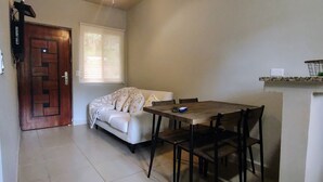 Una habitación pequeña y acogedora con una puerta de madera, un sofá blanco, una mesa de comedor con sillas y un estante con una cesta.