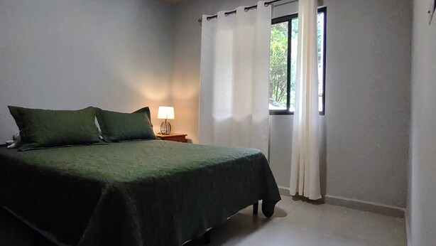 Un dormitorio con cama, mesita de noche, lámpara y ventana con cortinas.