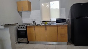 Una cocina compacta con armarios de madera, un refrigerador negro, un microondas, una cafetera y una estufa.