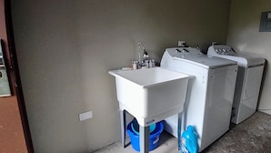 Un área de lavandería con un lavabo, dos lavadoras y un cubo azul.