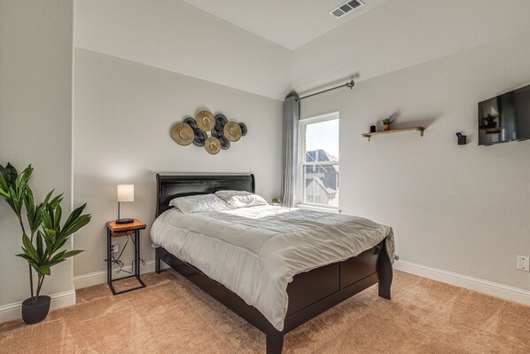 A bedroom with a bed, bedside lamp, potted plant, and a wall-mounted TV. - Spacious Texas Vacation Rental w/ Community Pool (Mansfield)