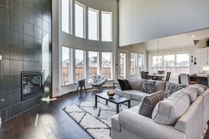 A spacious living room with a fireplace, large windows, a modern sofa set, and a dining area. - Spacious Texas Vacation Rental w/ Community Pool (Mansfield)
