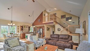 Ein geräumiges Wohnzimmer mit einer braunen Ledersofa, gemusterten Sesseln und einem Holztisch. Eine Treppe mit Holzwand führt auf eine obere Ebene.