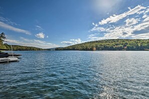 A calm lake with a dock and a forested hill in the background. - Inviting Lakefront Home: Seasonal Boat Dock! (Holden)