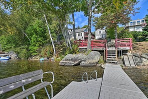 A wooden dock leading to a rocky shore with a bench and a red railing. - Inviting Lakefront Home: Seasonal Boat Dock! (Holden)