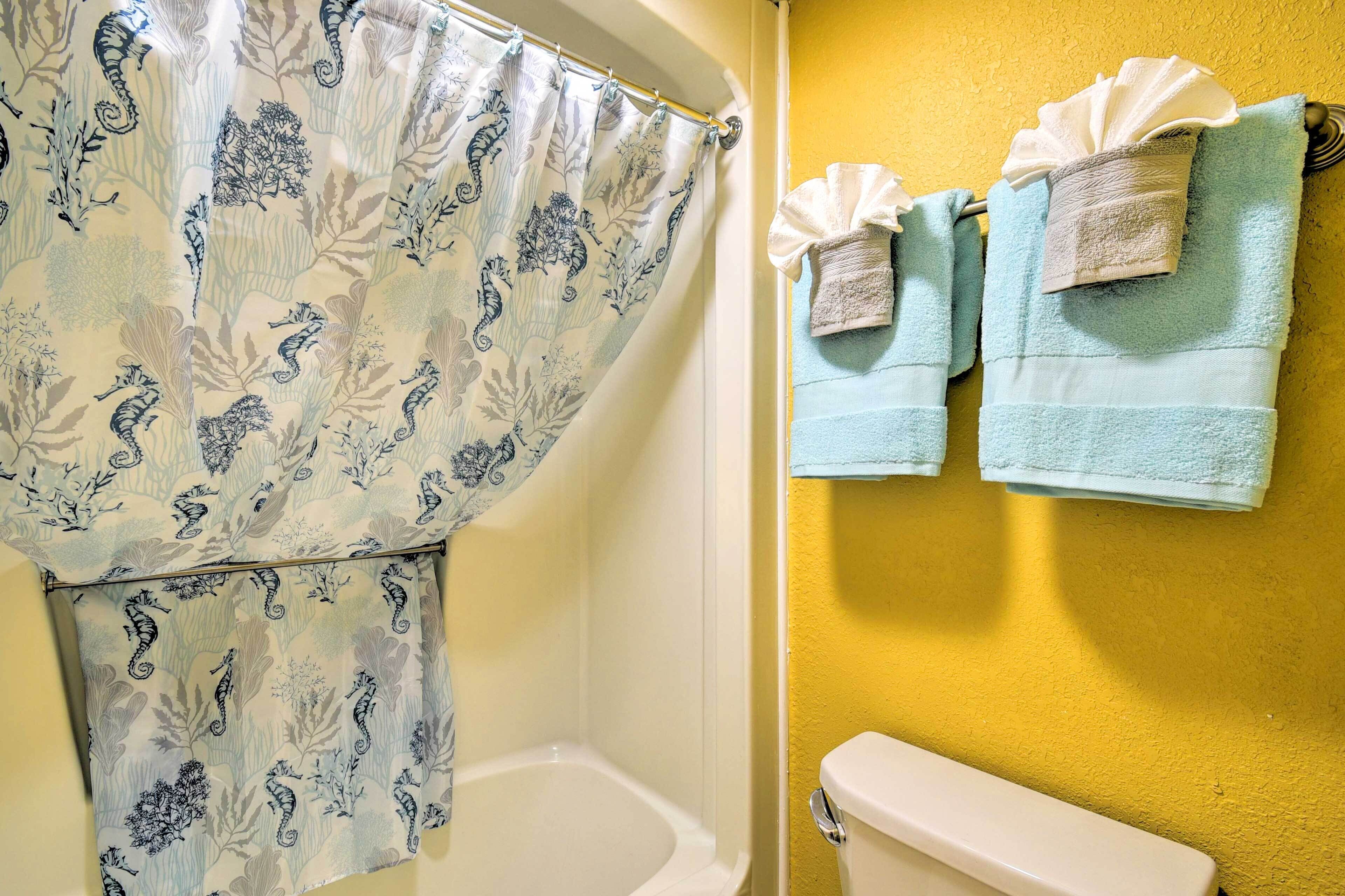 Een badkamer met een douchegordijn met een patroon van zeepaardjes en bladeren, een wit toilet en twee handdoeken die aan een handdoekhouder hangen.
