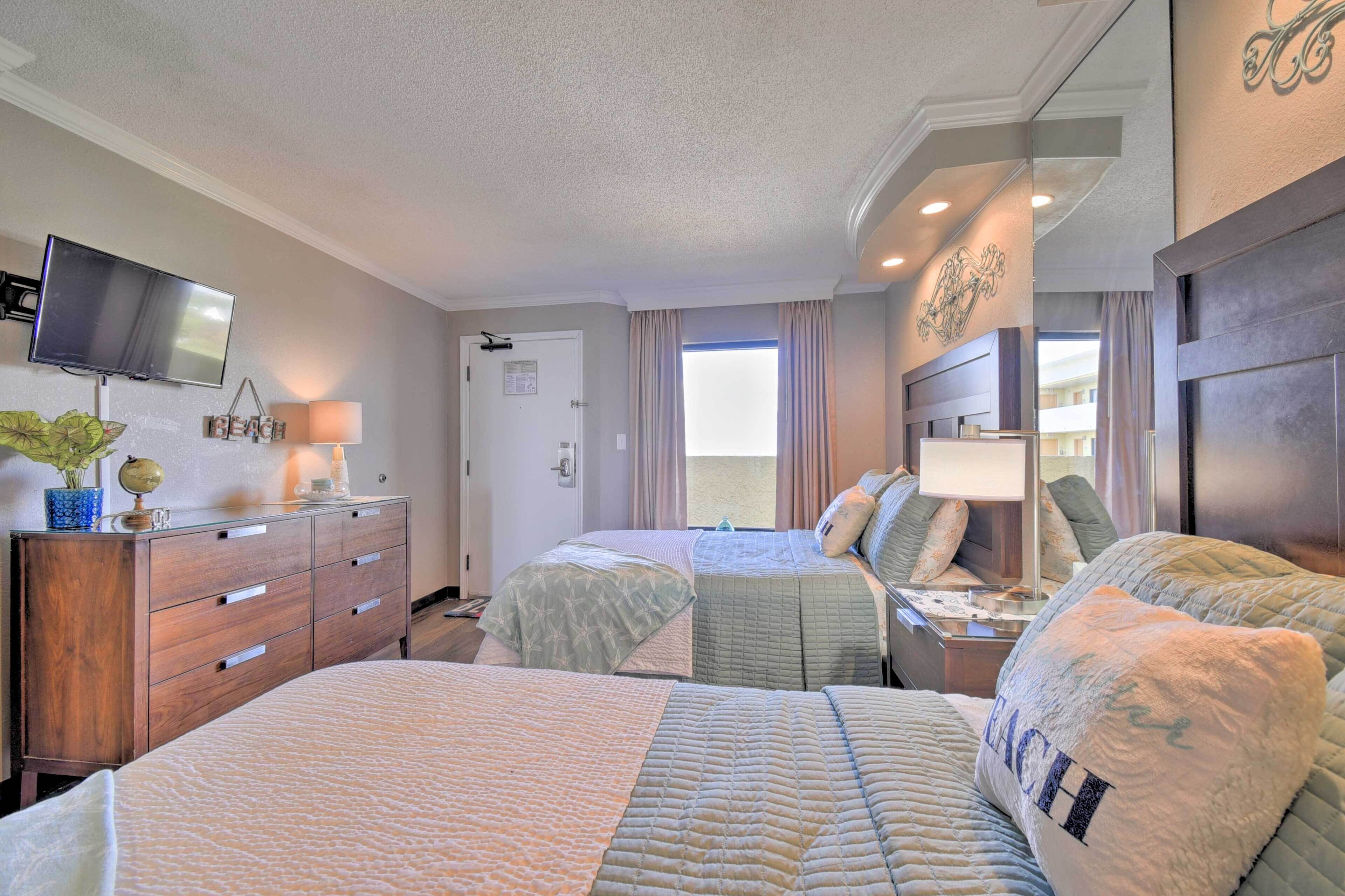 A hotel room with two beds, a TV, a dresser, and a window with curtains.