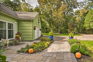 A green house with a patio, potted plants, and a pathway leading to a lawn.