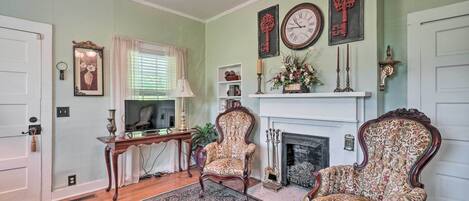 A traditional living room with a fireplace, two ornate chairs, a large clock, and a decorative key on the wall.