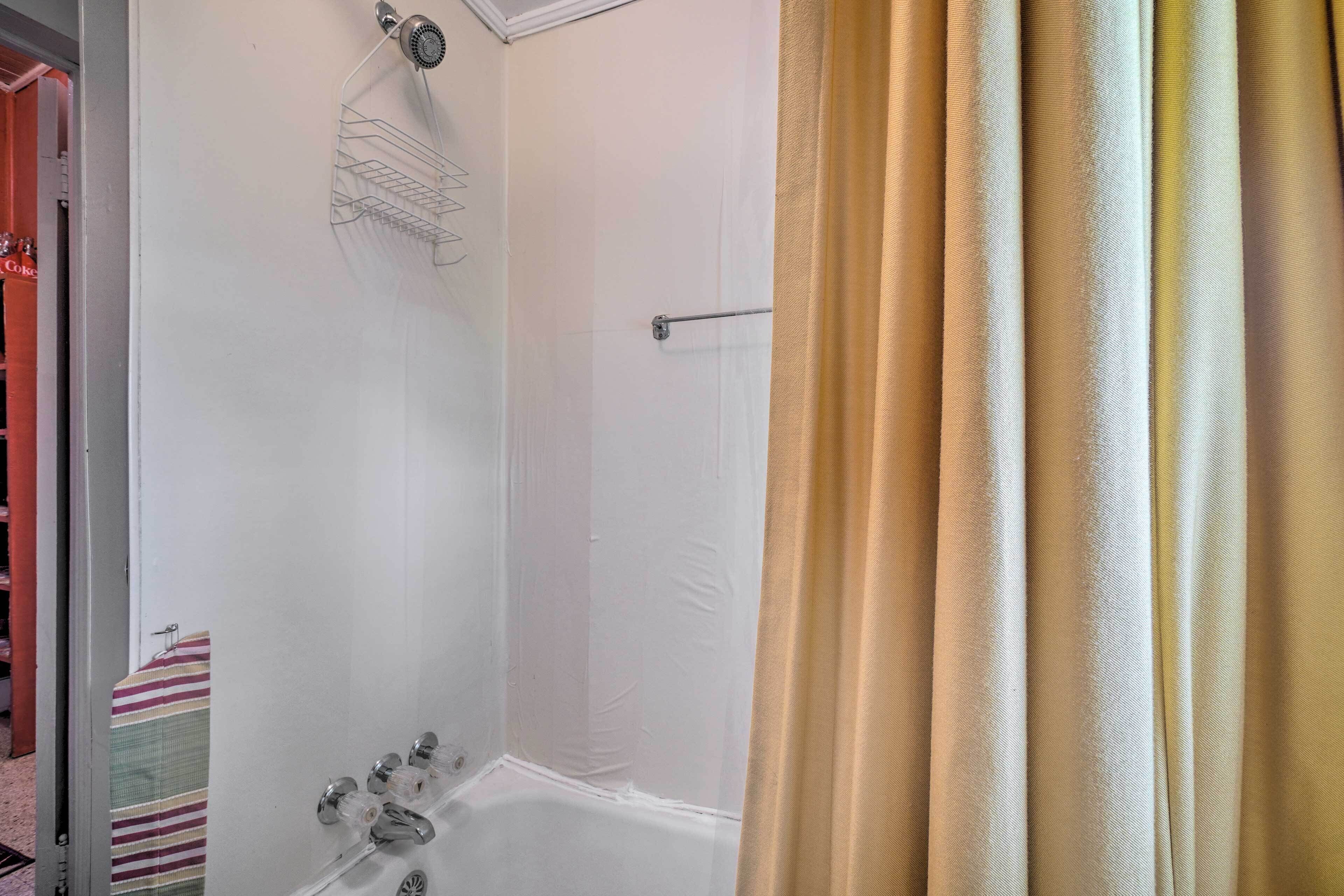 A shower area with a showerhead, a towel rack, and a curtain.