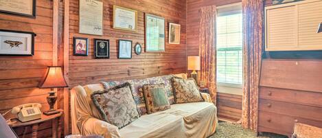 Una habitación acogedora con pared de madera, un sofá, una silla, una lámpara y un ventanal con cortinas.