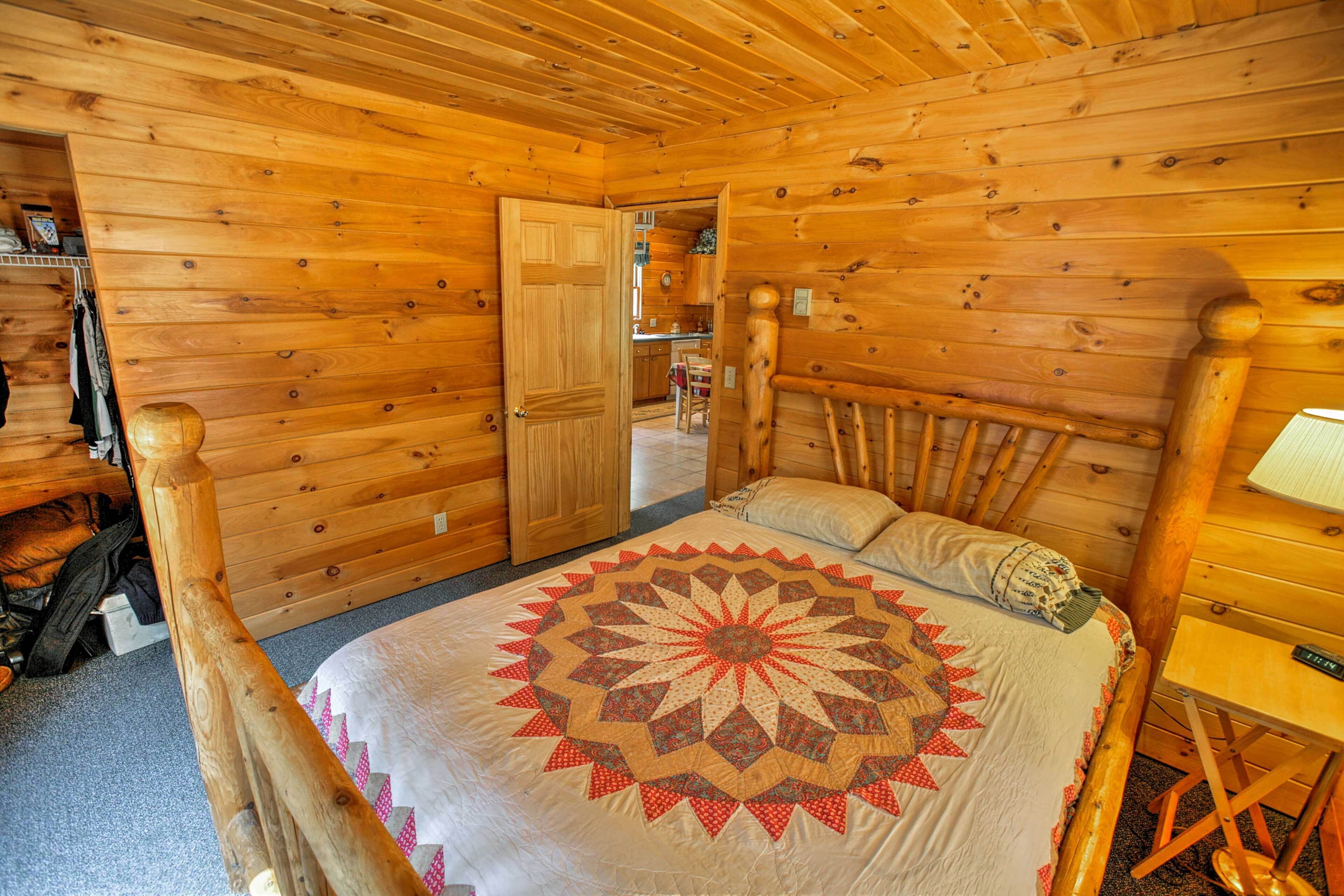 A wooden cabin bedroom with a bed, a wooden headboard, a quilt, and a small table.