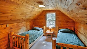 Een gezellig vakantiehuisje met twee houten bedden, een kleine tafel en een raam met uitzicht op het bos.