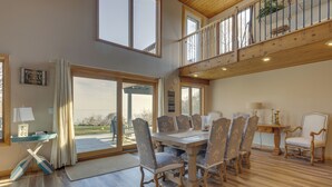 A spacious dining area with a wooden table and upholstered chairs, large windows, and a view of the outdoors. - Amazing Rocky Point Retreat Overlooking the Sound! (Rocky Point)