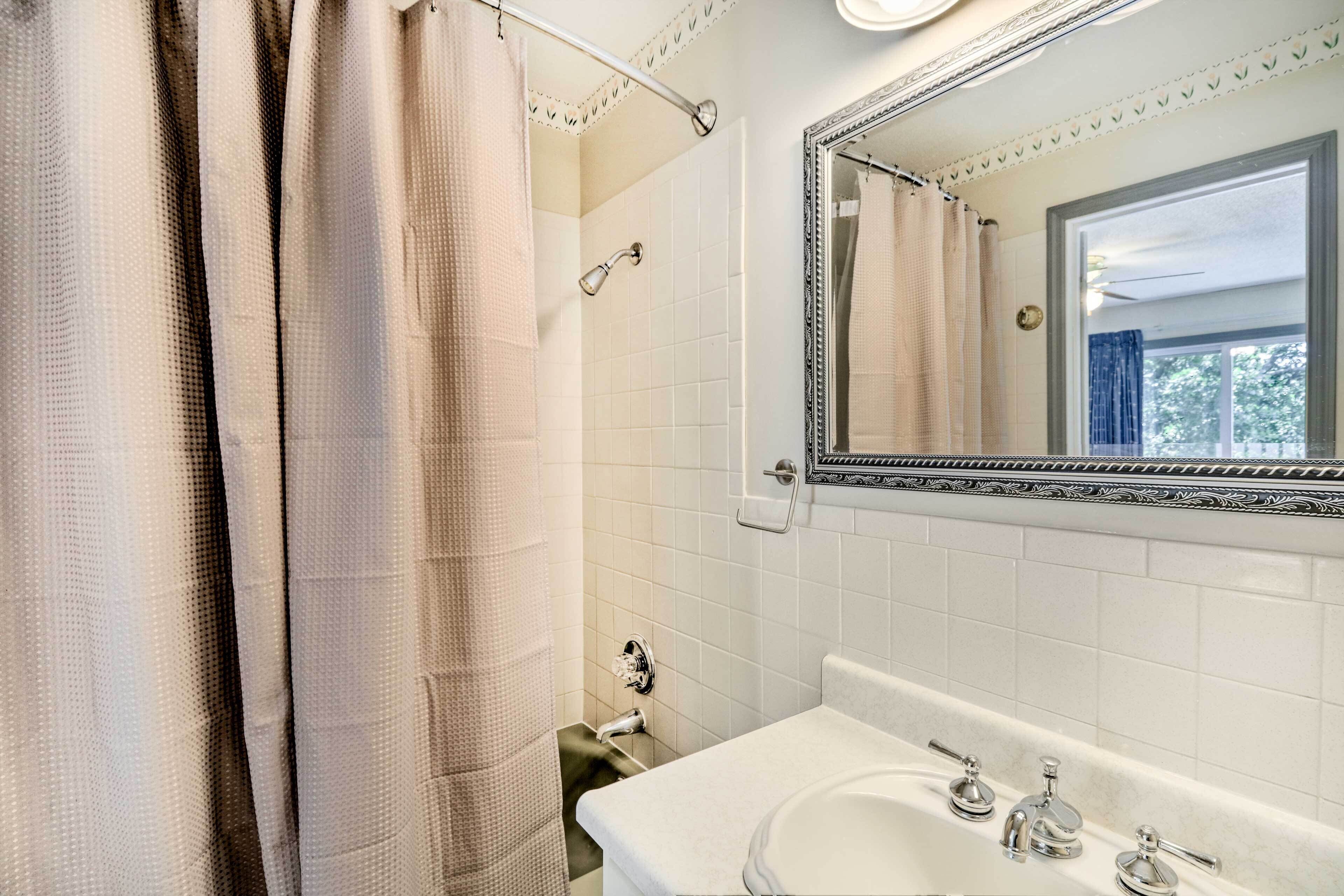 Une salle de bain avec un lavabo blanc, deux robinets, un miroir avec un cadre décoratif et un rideau de douche.