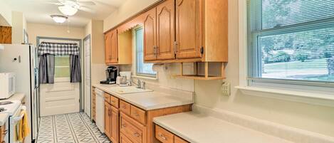 A compact kitchen with wooden cabinets, a built-in sink, and a window with blinds.