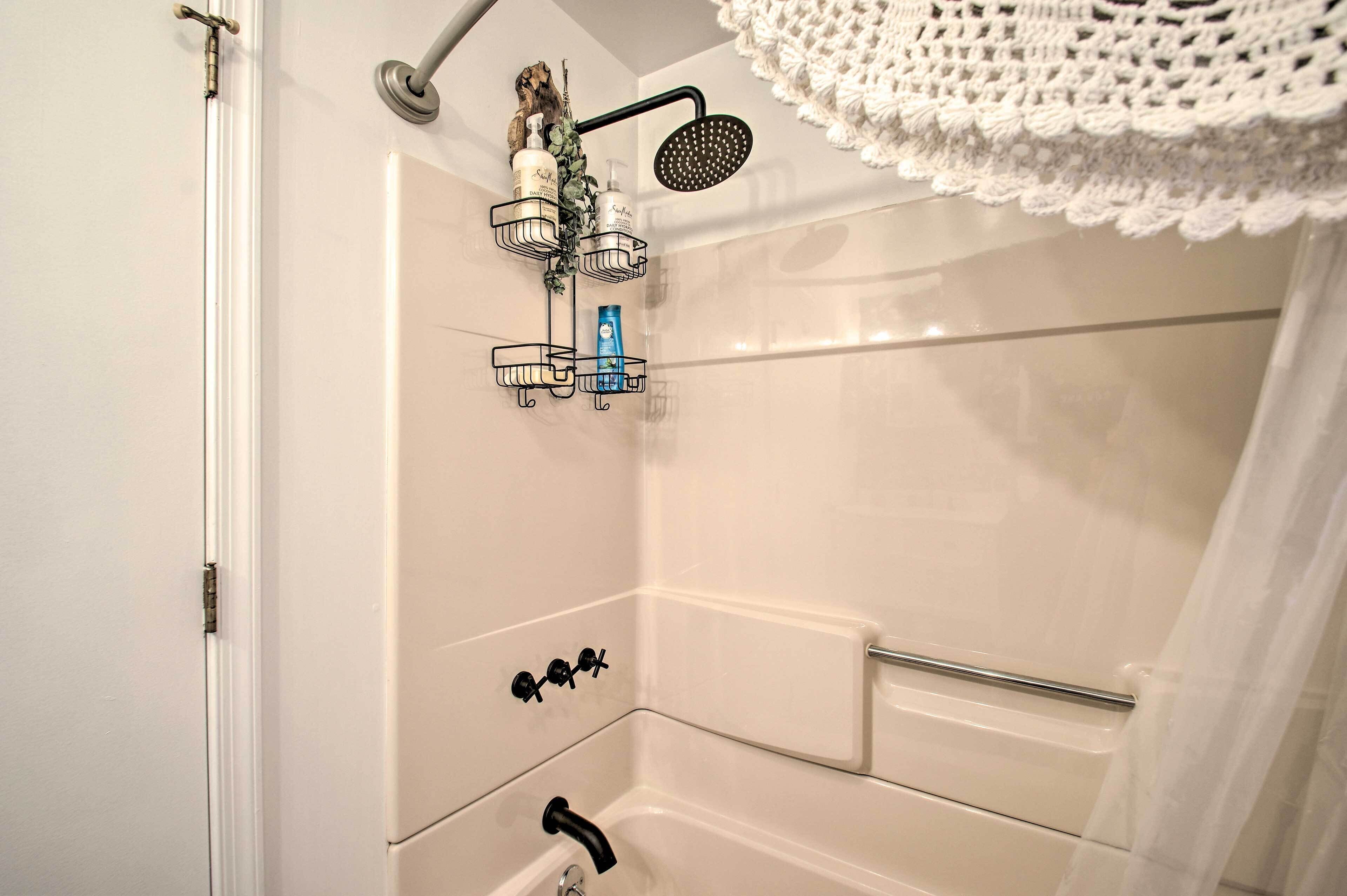 A shower area with a rain showerhead, a towel rack, and a soap dispenser.