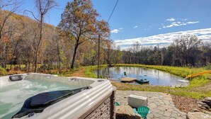 A hot tub by a pond with a dock, surrounded by trees and a clear sky. - Stoney Creek Cottage: Waterfront Hot Tub, Fire Pit (Nellysford)