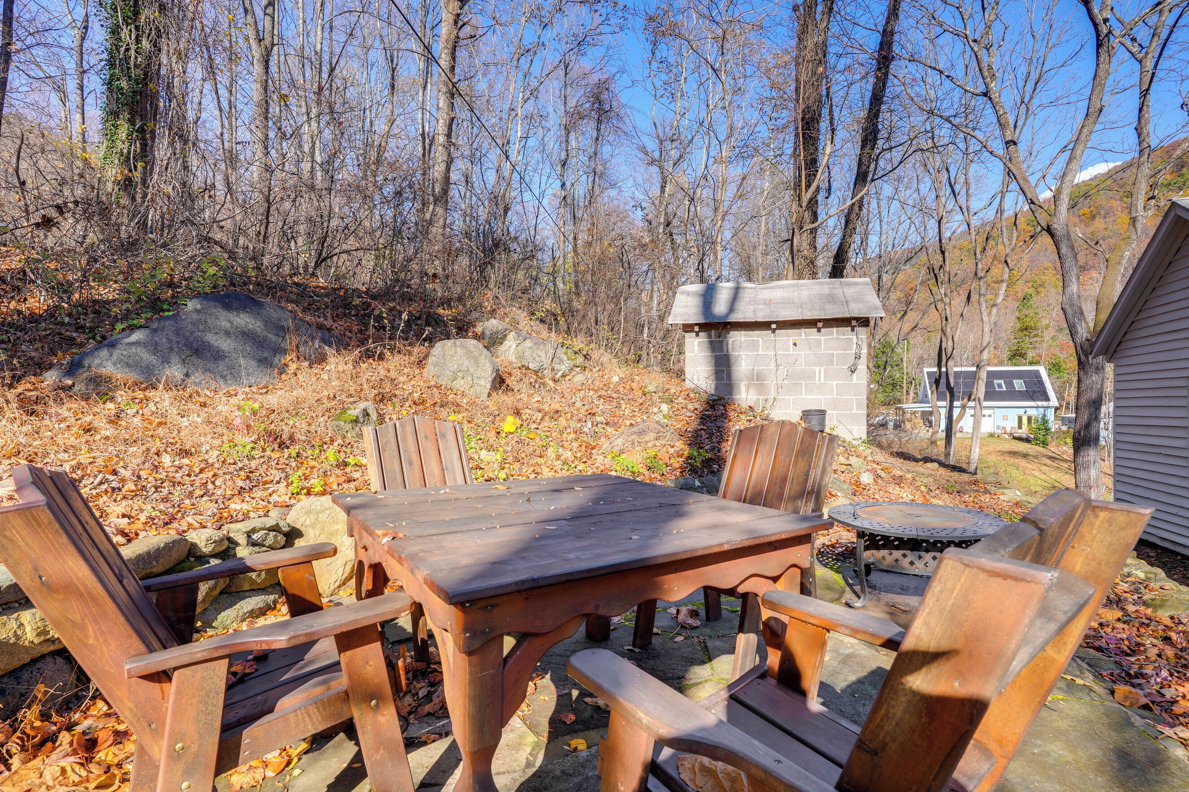 An outdoor wooden table and chairs set on a stone patio with a stone fireplace and a stone building in the background.