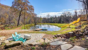 A pond with a playground, stone patio, and chairs. - Stoney Creek Cottage: Waterfront Hot Tub, Fire Pit (Nellysford)
