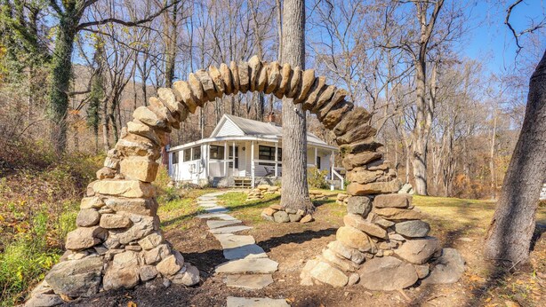 A stone archway leading to a house surrounded by trees. - Stoney Creek Cottage: Waterfront Hot Tub, Fire Pit (Nellysford)