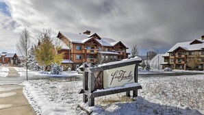 A snow-covered sign for 'FirstTracks' in front of a lodge with multiple stories and a snow-covered roof. - Wildhorse Meadows Studio w/ Resort Gondola Access! (Steamboat Springs)