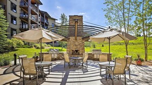 An outdoor patio with a stone fireplace, outdoor furniture, and umbrellas. - Wildhorse Meadows Studio w/ Resort Gondola Access! (Steamboat Springs)