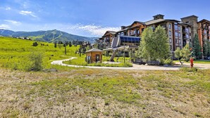 A hotel with multiple floors, outdoor pathways, and a view of green hills and mountains. - Wildhorse Meadows Studio w/ Resort Gondola Access! (Steamboat Springs)
