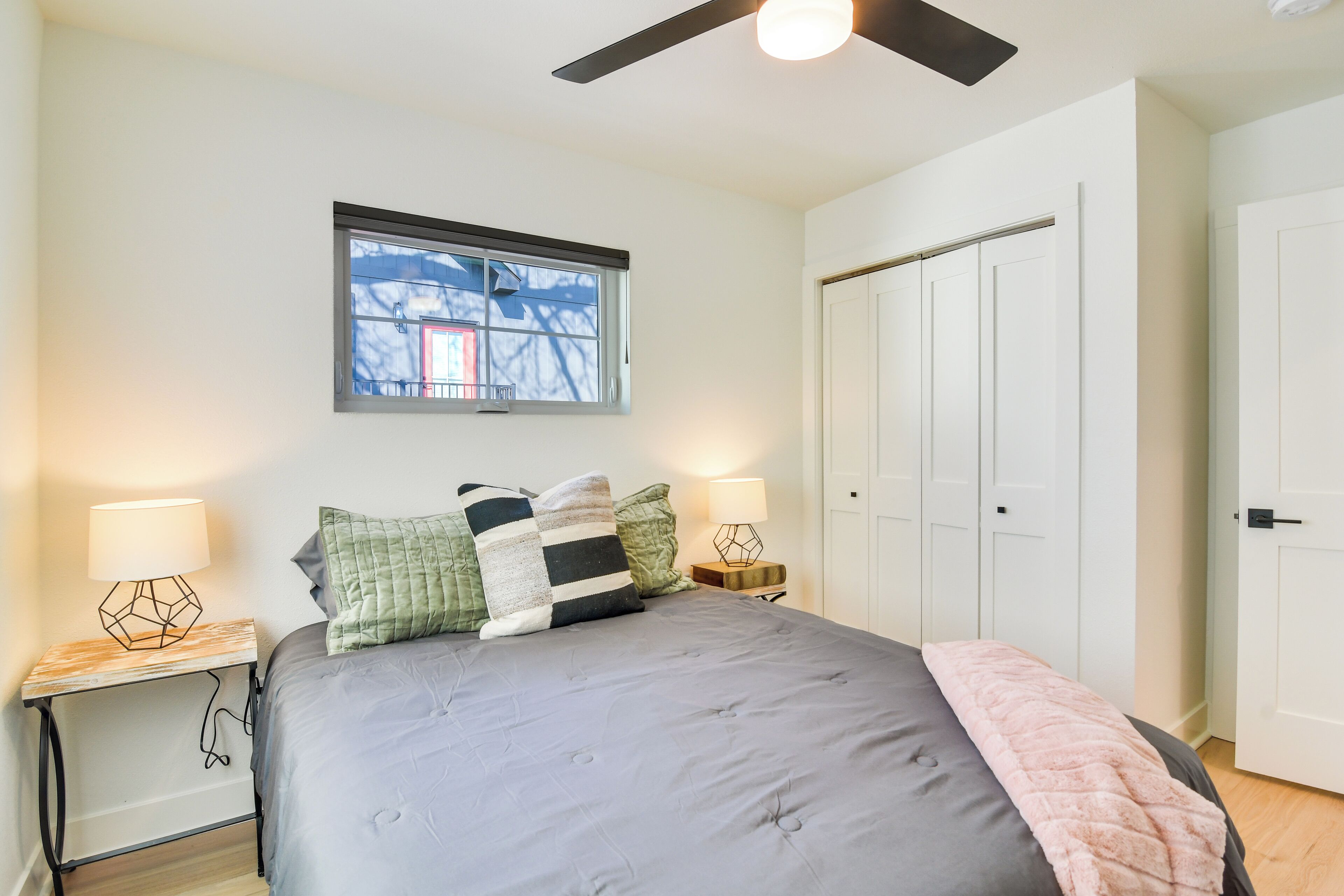 Un dormitorio con cama, dos mesitas de noche con lámparas, una ventana y un ventilador de techo.