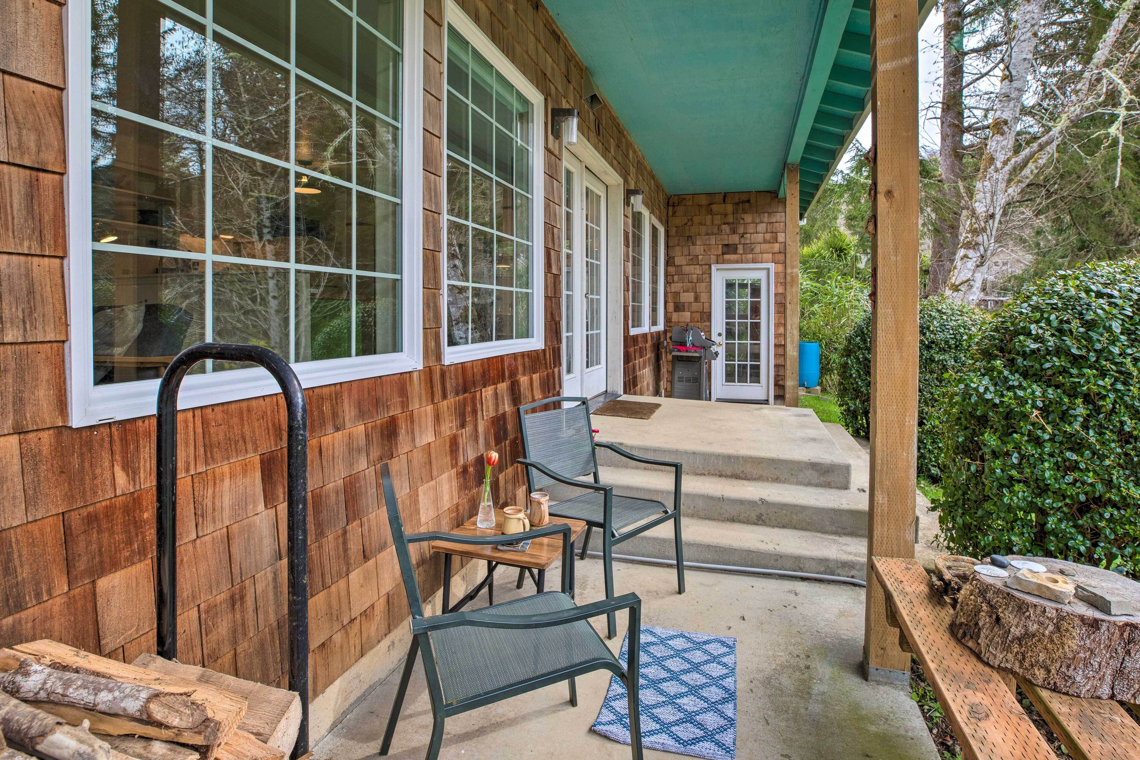 A wooden exterior with large windows, a covered porch with chairs, and a barbecue grill.