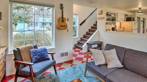 Ein Wohnzimmer mit einer Couch, einem Sessel, einer Gitarre und Blick auf eine Treppe, die zur Küche führt.