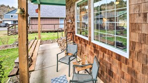 Ein überdachter Patio-Bereich mit zwei Stühlen und einem Tisch, eine Holzterrasse und Blick auf ein Nachbarhaus.