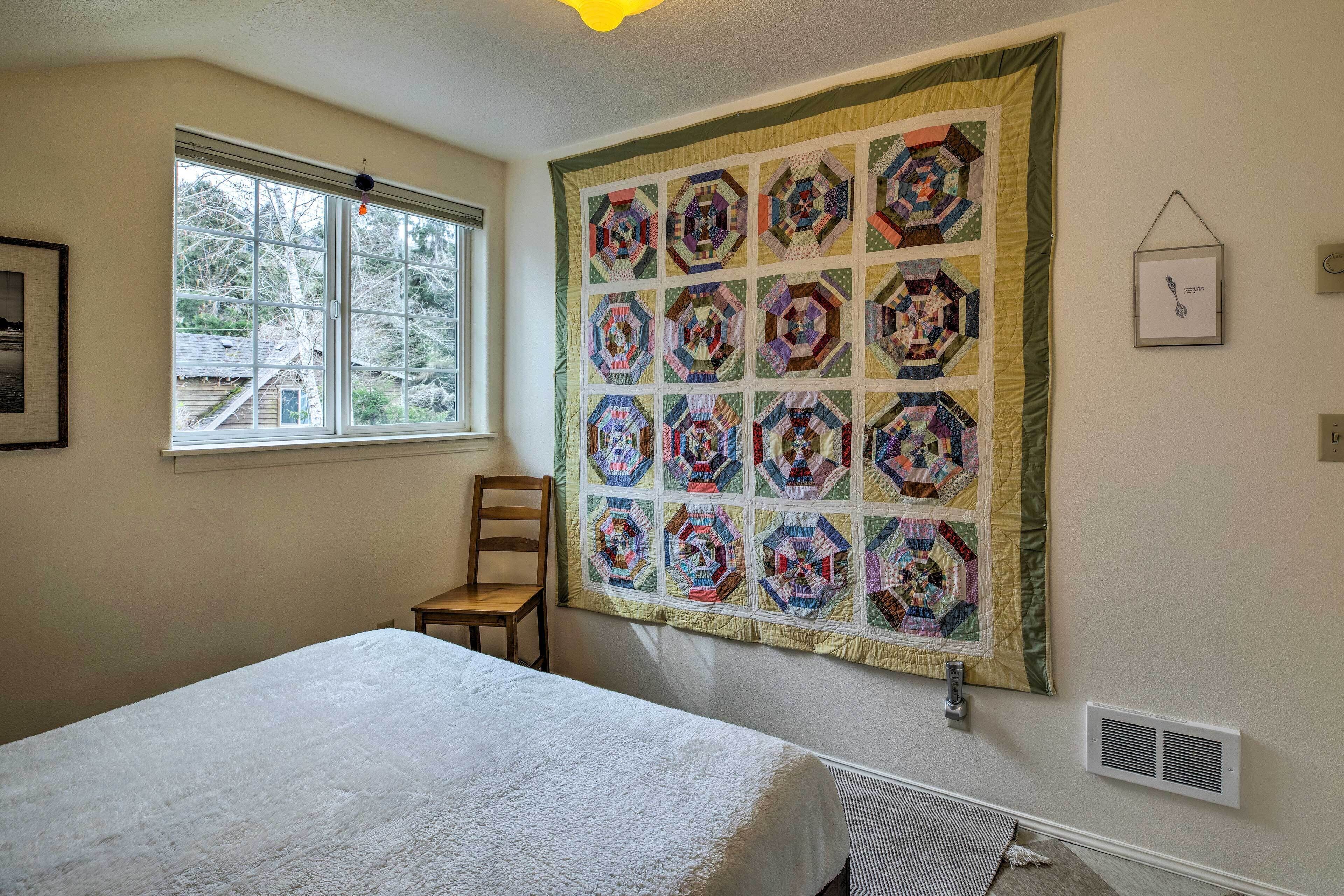 A bedroom with a large quilt, a window, a chair, and a bed.