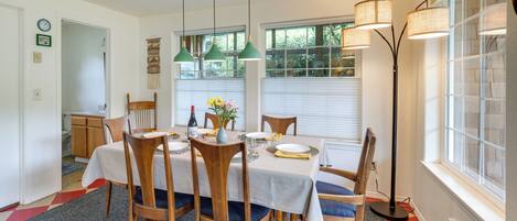 A dining area with a table set for four, surrounded by wooden chairs. There are hanging green pendant lights above the table.