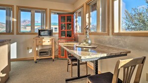 A kitchen with a granite countertop, wooden cabinets, a microwave, and a red cabinet with glass doors. - Charming Studio - 3 Miles From Kolob Canyons! (New Harmony)