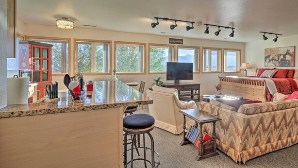 A spacious living area with a kitchen counter, bar stools, a sofa, and a television. - Charming Studio - 3 Miles From Kolob Canyons! (New Harmony)