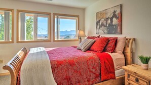 A bedroom with a large bed, multiple windows, a wooden headboard, a nightstand, and a painting on the wall. - Charming Studio - 3 Miles From Kolob Canyons! (New Harmony)