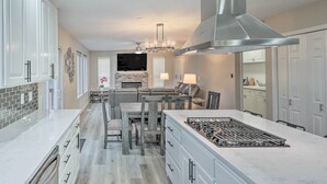 A modern kitchen with white cabinetry, a large island with a gas stove, and a dining area with a chandelier. - Spacious Kent Home: Great for Large Families! (Kent)