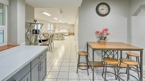 A modern kitchen with a white countertop, a wooden dining table with bar stools, and a clock on the wall. - Spacious Kent Home: Great for Large Families! (Kent)