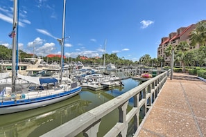 Uma marina com barcos atracados, um calçadão de madeira e um edifício com telhado vermelho ao fundo.