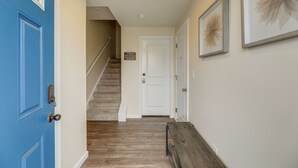 Un pasillo con una puerta azul, una puerta blanca y una escalera que lleva a otra habitación.