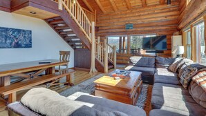 A log cabin interior with a wooden staircase, a sofa, a dining table, and a television. - Access to Rocky Mtn Nat'l Park: Grand Lake Cabin (Grand Lake)