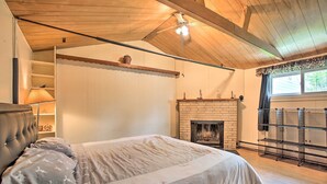Ein Schlafzimmer mit Bett, Kamin, Deckenventilator und einem Fenster mit Vorhängen.
